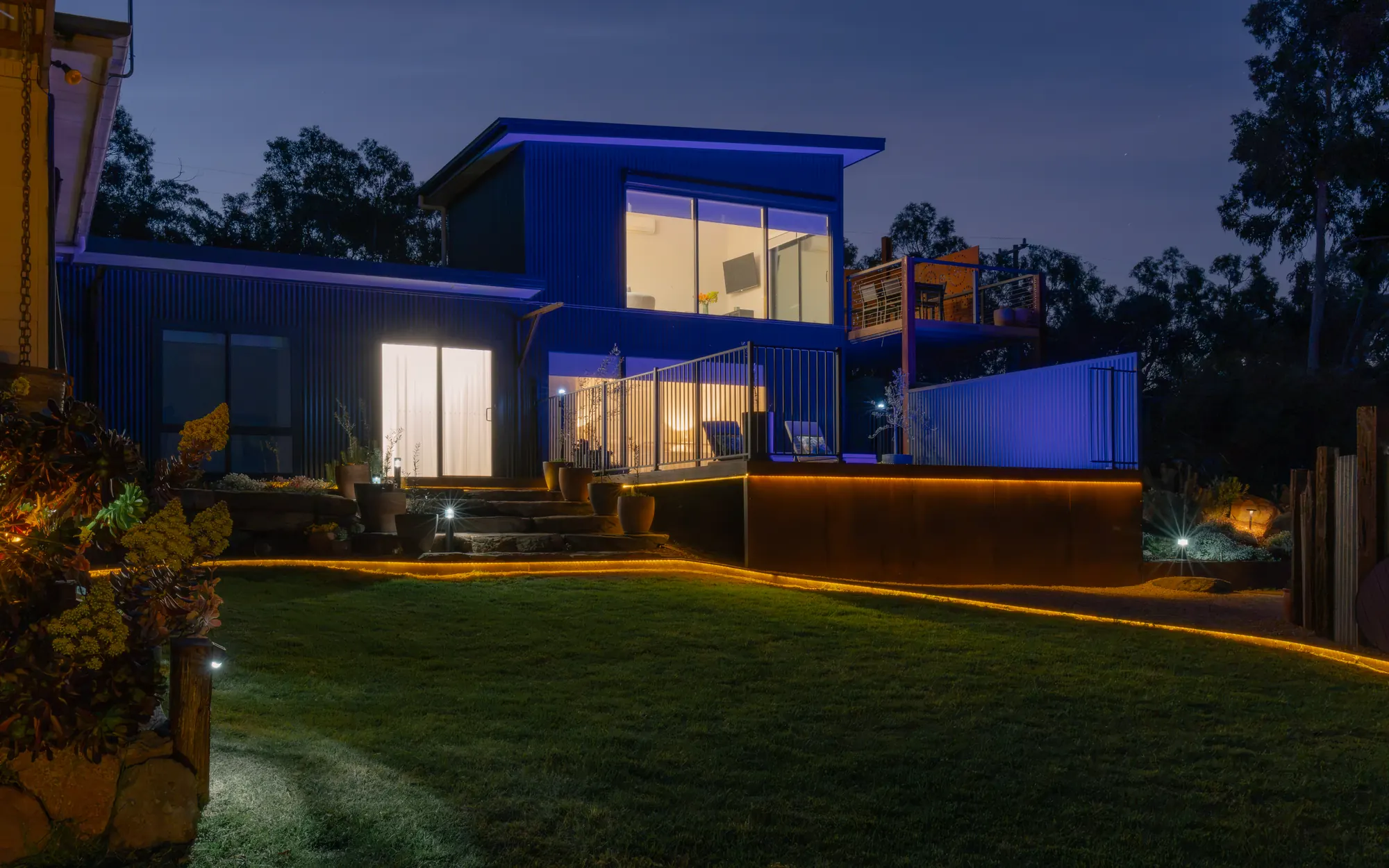 The two-storey accommodation at dusk, lit inside and out, on the lawn under a deep blue sky